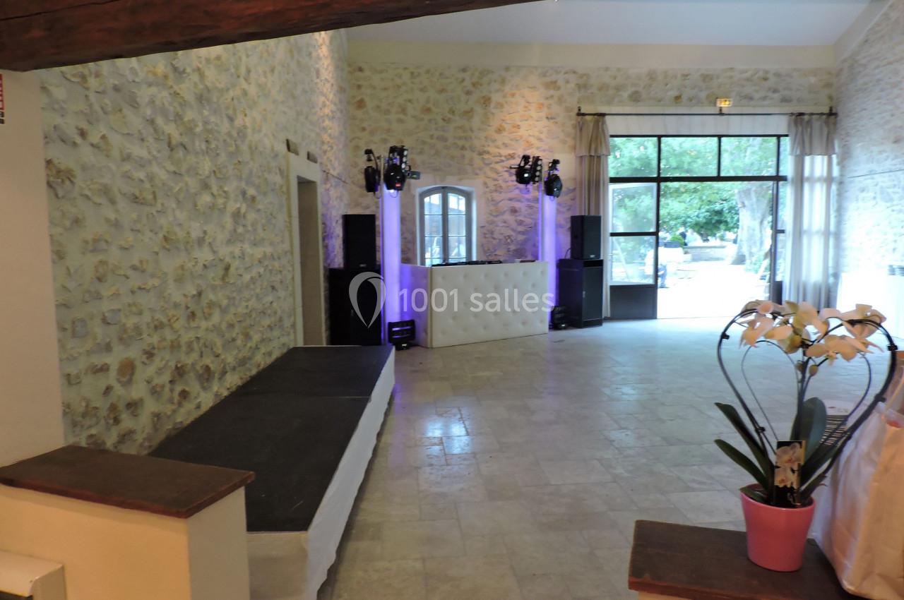 Salle en pierre avec une estrade, un espace DJ éclairé et une plante en pot près d'une grande baie vitrée donnant sur l…