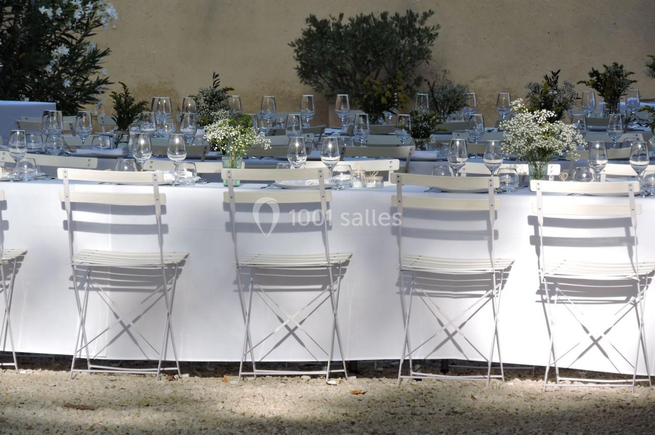 Table dressée en extérieur avec nappes blanches, chaises pliantes, verres, couverts et décorations florales.
