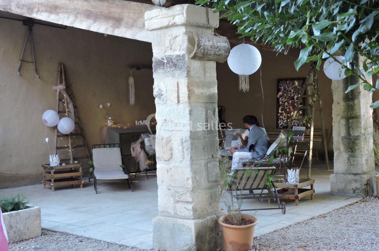 Terrasse couverte rustique avec mobilier en bois, décorations suspendues et une personne assise à une table.