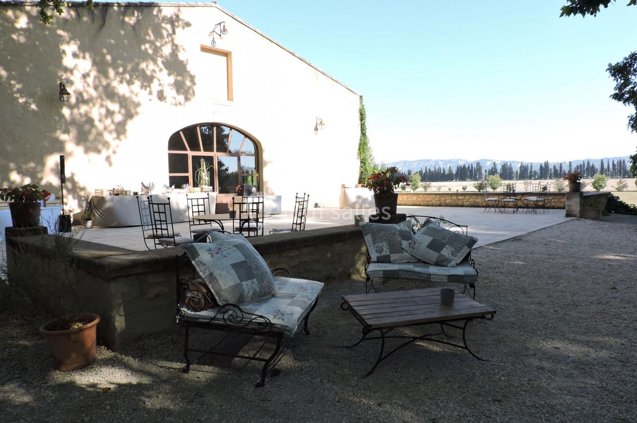 Terrasse ensoleillée avec mobilier de jardin, vue sur un paysage rural et bâtiment en pierre clair.