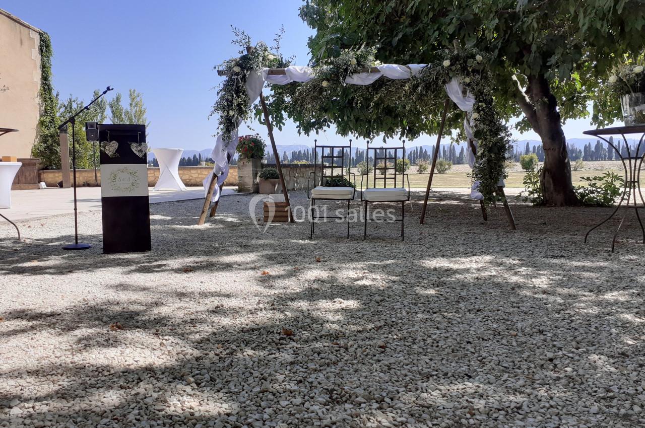Arche décorée pour une cérémonie en plein air, entourée de chaises et d'arbres sous un ciel dégagé.