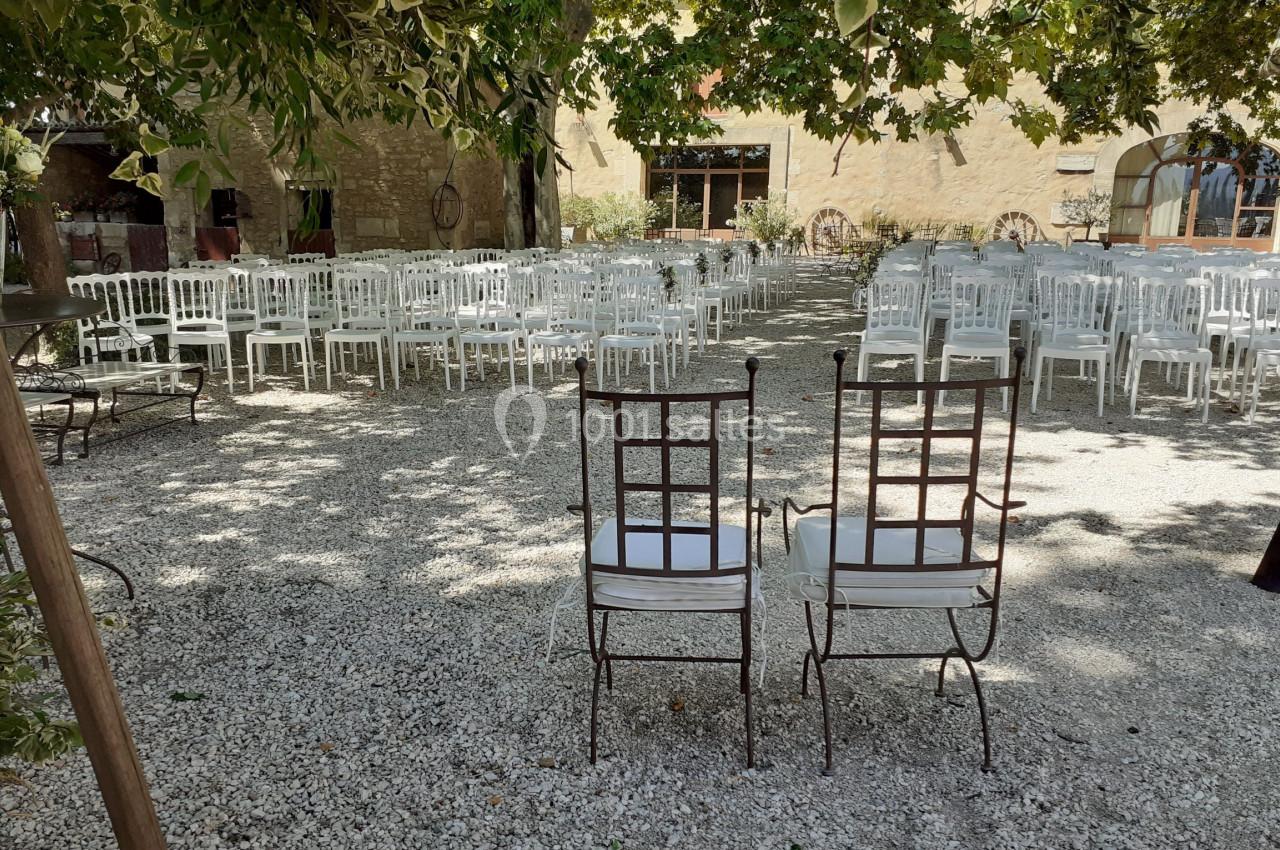 Chaises blanches alignées en extérieur sous des arbres, préparées pour un événement, avec deux chaises en premier plan.