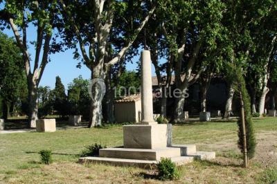 Colonne en pierre sur un socle dans un parc arboré, entourée de pelouse et d'arbres feuillus.