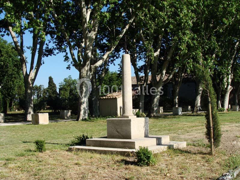 Colonne en pierre sur un socle dans un parc arboré, entourée de pelouse et d'arbres feuillus.