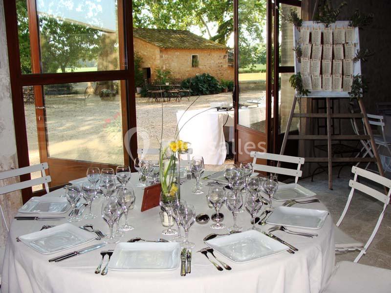 Table dressée avec vaisselle élégante et vase de fleurs jaunes, dans une salle lumineuse donnant sur un jardin.