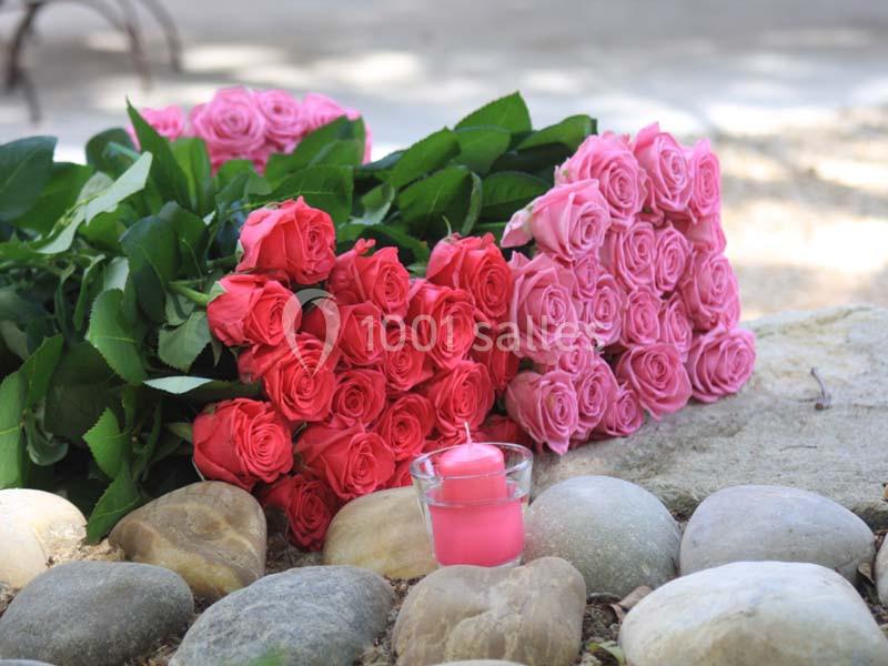 Bouquets de roses roses et rouges posés sur des galets, avec une bougie rose dans un photophore en verre.
