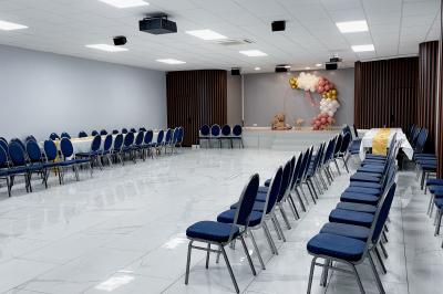 Salle de réception avec tables rondes couvertes de nappes blanches, chaises bleues et une scène avec rideaux bleus.
