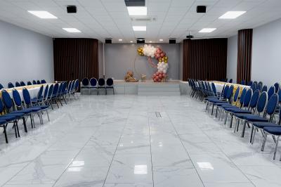 Salle de réception avec tables rondes couvertes de nappes blanches, chaises bleues et une scène avec rideaux bleus.