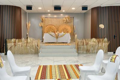 Salle de réception avec tables rondes couvertes de nappes blanches, chaises bleues et une scène avec rideaux bleus.