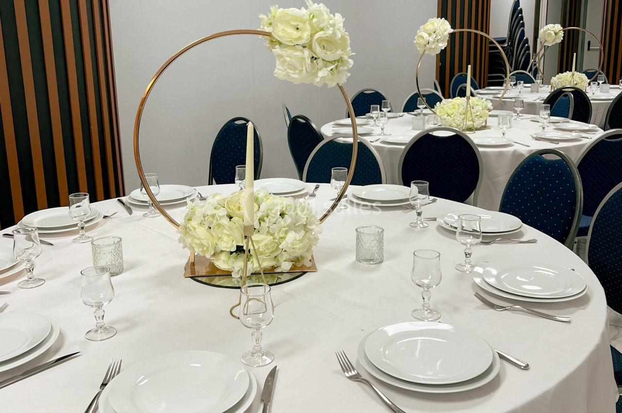 Table dressée avec nappes blanches, vaisselle, verres et centre de table floral circulaire dans une salle de réception.