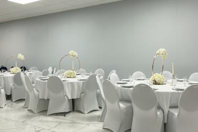 Salle de réception avec tables rondes couvertes de nappes blanches, chaises bleues et une scène avec rideaux bleus.