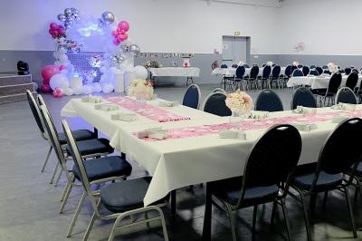 Salle de réception avec tables rondes couvertes de nappes blanches, chaises bleues et une scène avec rideaux bleus.