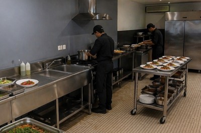 Cuisiniers en tenue noire préparant des plats dans une cuisine professionnelle équipée en inox.