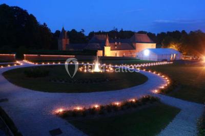 Cour pavée éclairée par des bougies et lumières chaudes, avec un bâtiment historique en arrière-plan, de nuit.