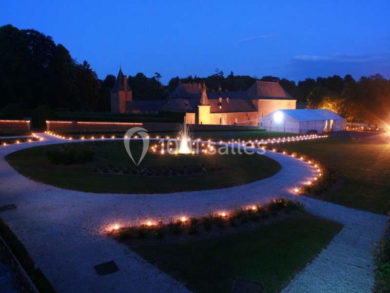 Jardin éclairé de nuit avec une fontaine centrale, allées lumineuses et un bâtiment en arrière-plan.