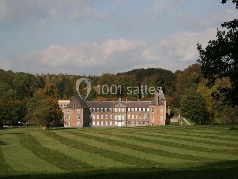 Bâtiment en briques entouré de vastes pelouses et d'arbres, sous un ciel partiellement nuageux.