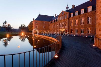 Cour pavée éclairée par des bougies et lumières chaudes, avec un bâtiment historique en arrière-plan, de nuit.