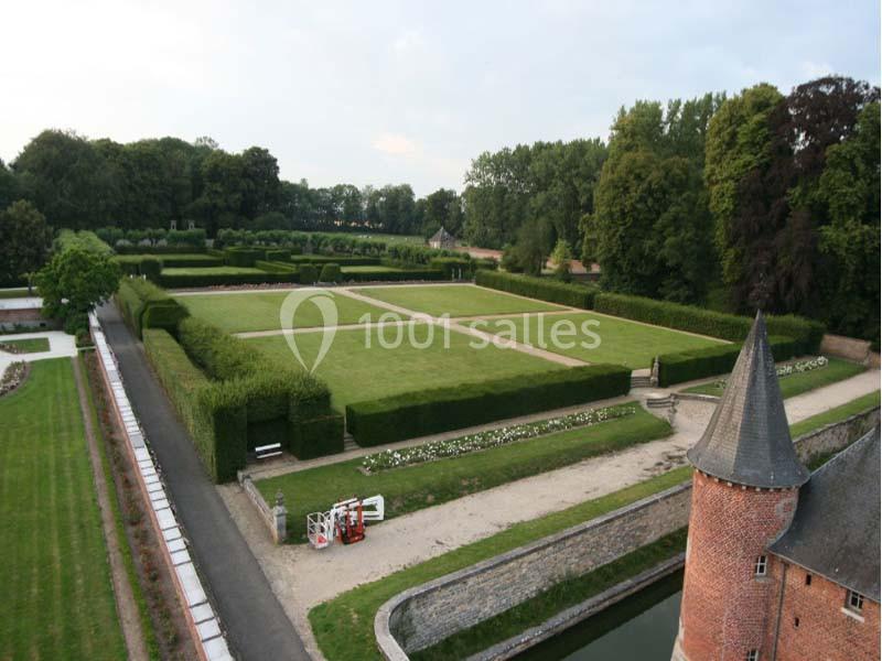 Vue aérienne d'un jardin géométrique entouré de haies, avec un bâtiment en briques et un fossé au premier plan.