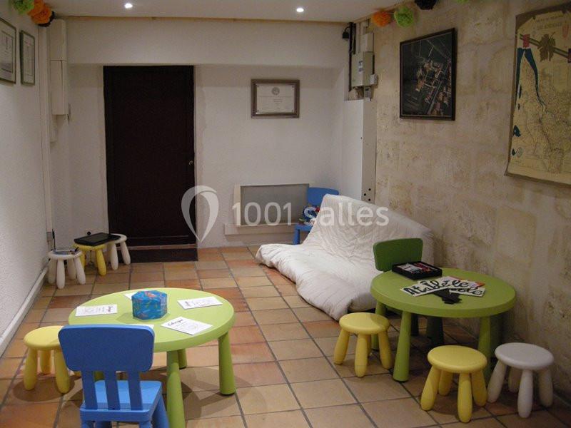 Salle d'attente avec tables et chaises colorées pour enfants, canapé blanc et décoration murale minimaliste.