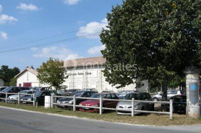 Parking devant un bâtiment en pierre marqué ’Château Saint Ahon’, entouré d'arbres et sous un ciel dégagé.