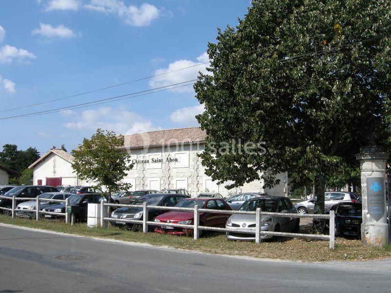 Parking devant un bâtiment en pierre marqué ’Château Saint Ahon’, entouré d'arbres et sous un ciel dégagé.
