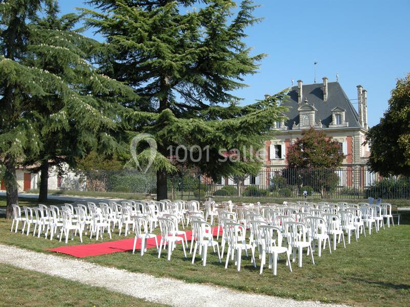 Chaises blanches disposées en extérieur sur une pelouse, face à un manoir, avec tapis rouge et arbres en arrière-plan.