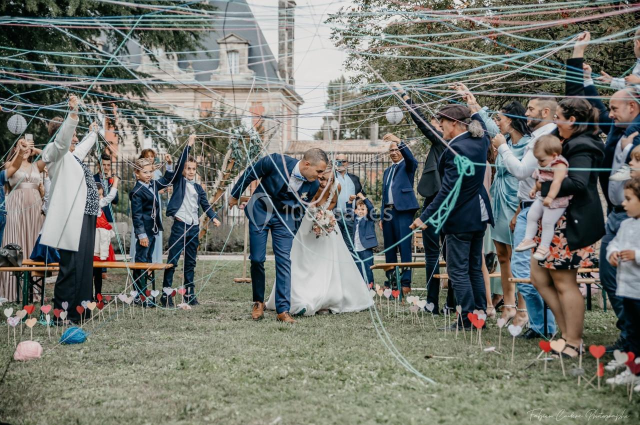 Un couple de mariés s'embrasse sous une haie d'honneur faite de fils colorés tendus par des invités.