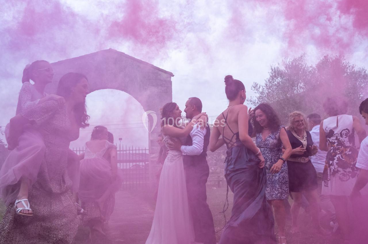 Groupe de personnes célébrant un mariage dans un nuage de fumée rose, près d'une arche en pierre en extérieur.