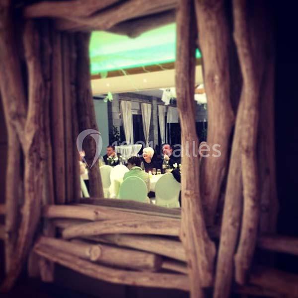 Reflet d'une salle de réception avec des convives assis, vu à travers un cadre en bois rustique.