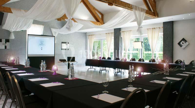 Salle de réunion lumineuse avec grandes fenêtres, tables noires disposées en U, écran de projection et décoration élégante.