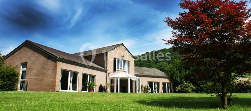 Maison en briques avec de grandes fenêtres, entourée d'un jardin verdoyant et d'un arbre au feuillage rouge.