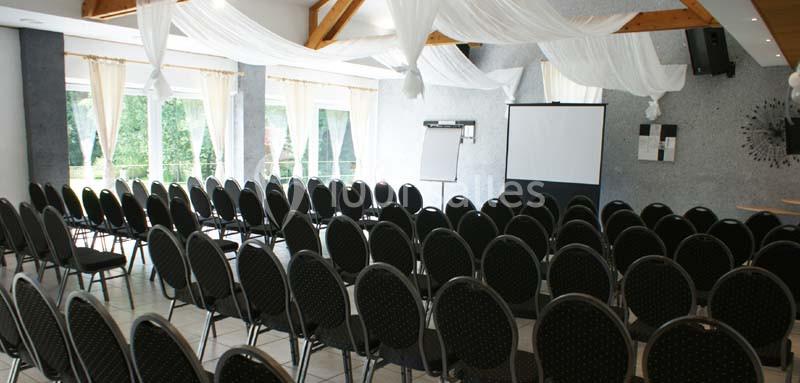 Salle de conférence lumineuse avec des rangées de chaises noires, un écran de projection et un tableau blanc.
