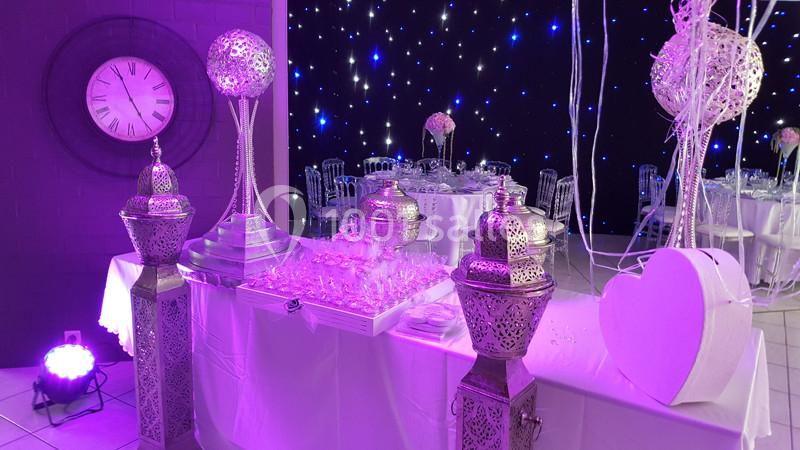 Décoration de salle de réception avec lanternes orientales, table dressée et éclairage violet sur fond étoilé.