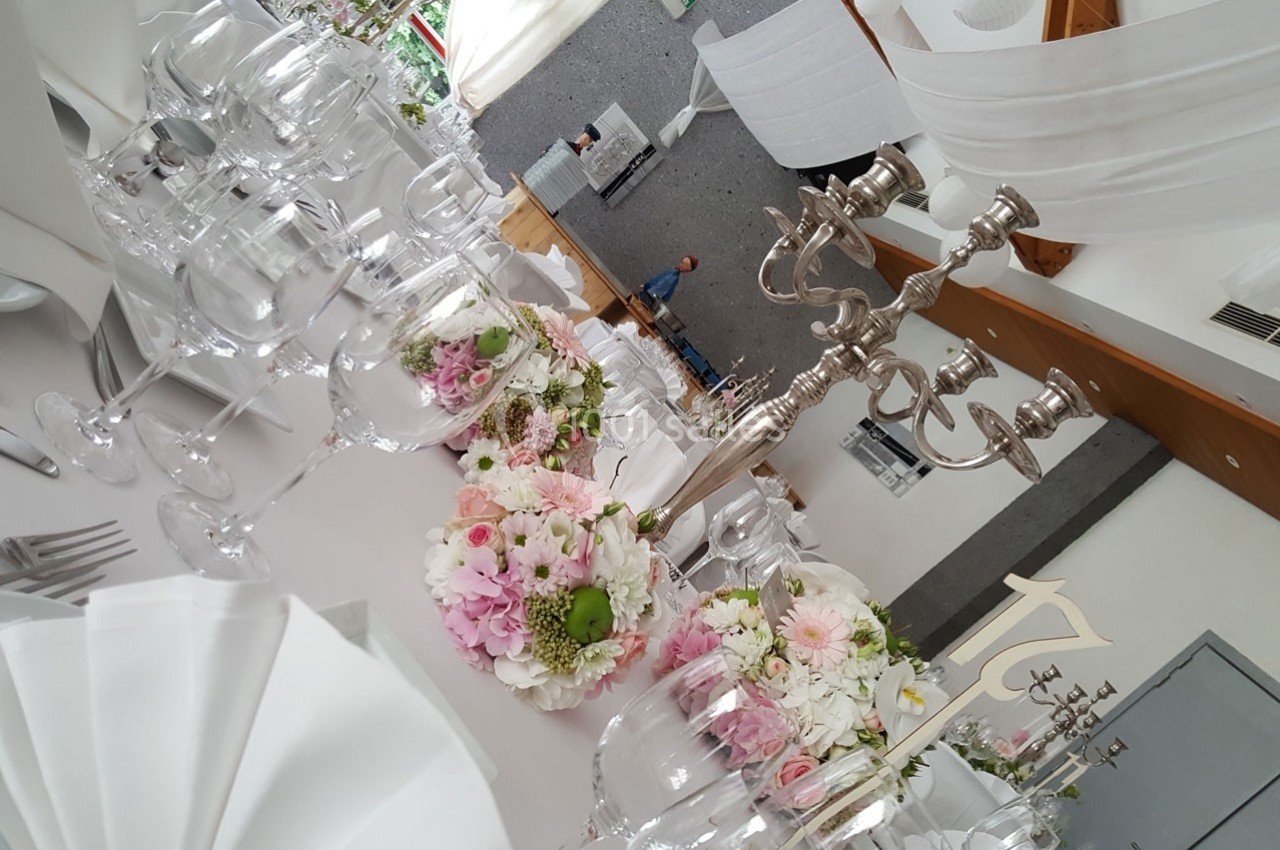 Table élégamment dressée avec des fleurs pastel, des chandeliers argentés et des verres en cristal dans une salle lumineuse.