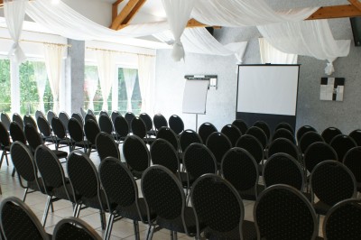 Miniature Location salle Flémalle (Liège) - Salons Ypsilon #28 Salle de conférence lumineuse avec des rangées de chaises noires, un écran de projection et un tableau blanc.