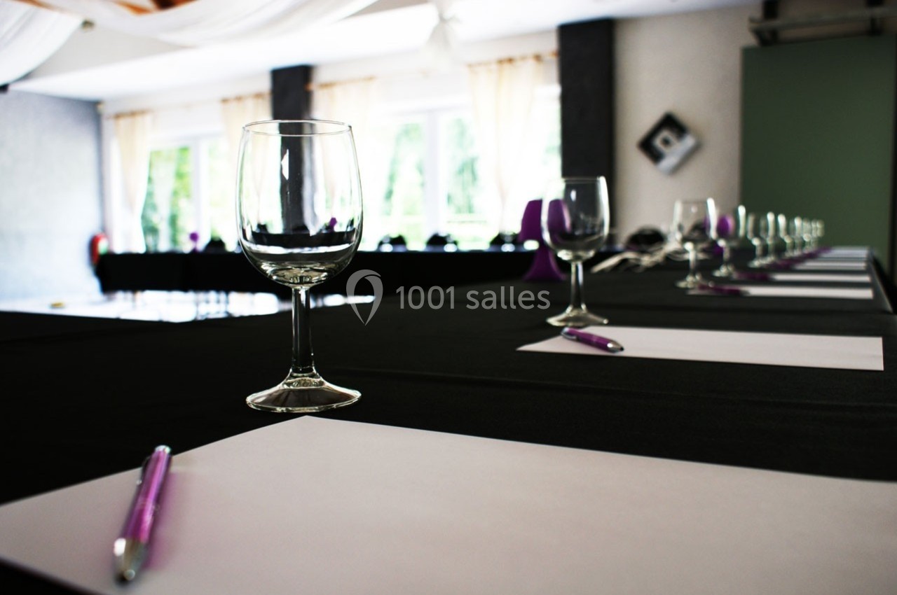 Salle de réunion avec des tables dressées, contenant des verres, des stylos et des feuilles blanches.