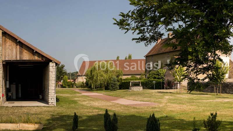 Vue d'une cour avec bâtiments ruraux, pelouse, allée pavée et arbres sous un ciel dégagé.
