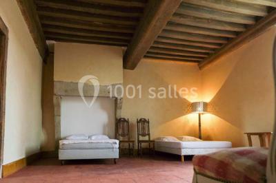 Salon rustique avec poutres apparentes, cheminée, mobilier en cuir et table basse en bois rouge dans un cadre chaleureux.