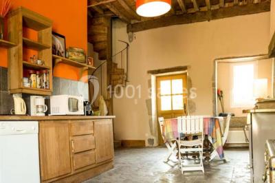 Salon rustique avec poutres apparentes, cheminée, mobilier en cuir et table basse en bois rouge dans un cadre chaleureux.