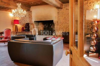 Salon rustique avec poutres apparentes, cheminée, mobilier en cuir et table basse en bois rouge dans un cadre chaleureux.