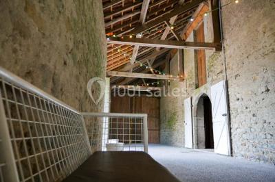 Salon rustique avec poutres apparentes, cheminée, mobilier en cuir et table basse en bois rouge dans un cadre chaleureux.