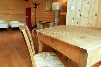 Salon rustique avec poutres apparentes, cheminée, mobilier en cuir et table basse en bois rouge dans un cadre chaleureux.