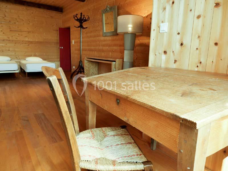 Chambre en bois avec un bureau, une chaise en paille, deux lits simples et un lampadaire près d'un mur en lambris.