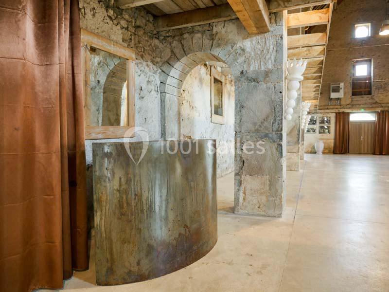 Comptoir métallique courbé dans un espace intérieur en pierre avec poutres en bois et rideaux marron.