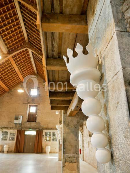 Sculpture blanche en forme de couronne et sphères fixée à un mur dans une grande salle avec charpente en bois apparente.