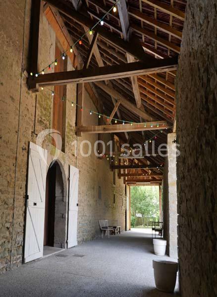 Passage couvert en pierre avec des guirlandes lumineuses suspendues, portes ouvertes et vue sur un jardin.