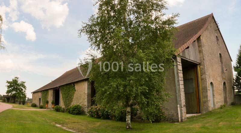 Bâtiment en pierre avec toit en pente, entouré de pelouse et d'arbres sous un ciel partiellement nuageux.