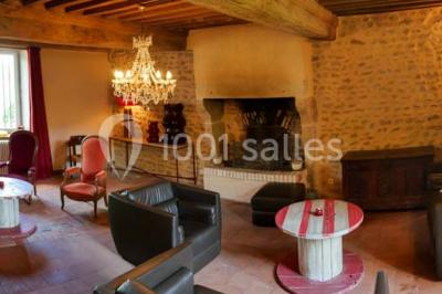 Salon rustique avec poutres apparentes, cheminée, mobilier en cuir et table basse en bois rouge dans un cadre chaleureux.