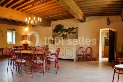 Salon rustique avec poutres apparentes, cheminée, mobilier en cuir et table basse en bois rouge dans un cadre chaleureux.