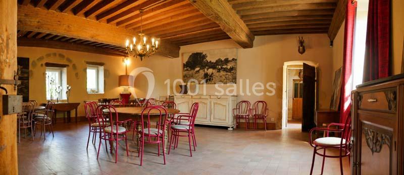 Salle à manger rustique avec poutres apparentes, chaises rouges, tables en bois et lumière naturelle entrant par les…